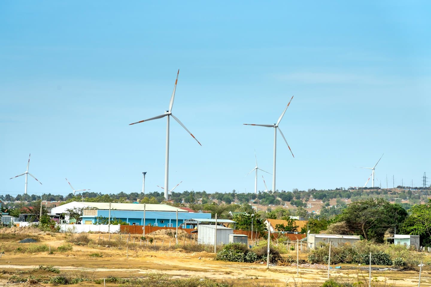 Turbine eoliche si ergono sopra gli edifici in un paesaggio rurale.